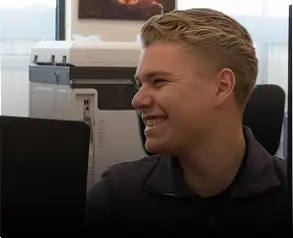 Een glimlachende jonge man met kort blond haar die een donkergrijs overhemd met kraag draagt.