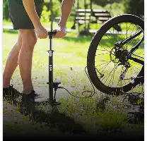 Zwarte fietspomp met een zilverkleurige handgreep en zwarte slang, rechtopstaand naast een fietswiel op gras.