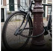 Zwarte fiets met een kettingslot dat om een roestbruine paal is gewikkeld.