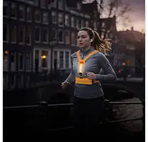 Een vrouw die een feloranje reflecterend hardloopvest draagt met zwarte bandjes en een centrale borstzak.