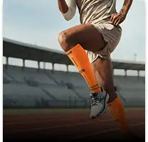 Felgekleurde oranje voetbalscheenbeschermers, gedragen door een atleet op een atletiekbaan.