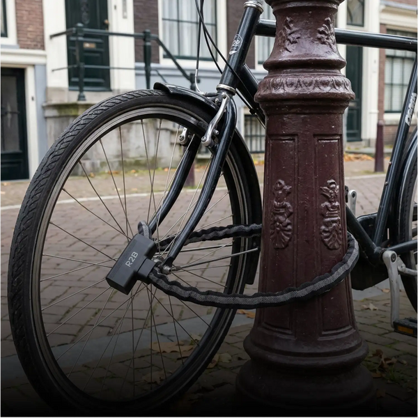Zwarte r2b-fietsslot met een dikke, gevlochten stalen ketting waarmee de fiets aan een sierlijke bruine paal is bevestigd.