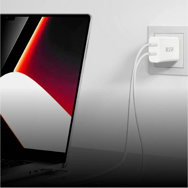Witte r2b-wandoplader met een strak, minimalistisch ontwerp die in een stopcontact naast een laptop is gestoken.