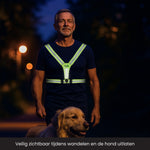 Man is een hond aan het uitlaten in het donker met een verlicht hardloopvest aan