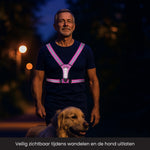 Man is een hond aan het uitlaten in het donker met een verlicht hardloopvest aan