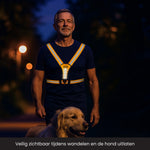 Man is een hond aan het uitlaten in het donker met een verlicht hardloopvest aan