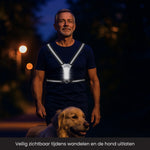 Man is een hond aan het uitlaten in het donker met een verlicht hardloopvest aan